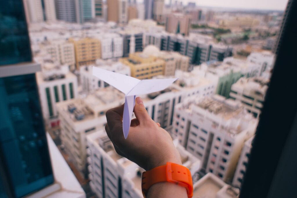 Mano con un avión de papel desde una ventana de un rascacielos